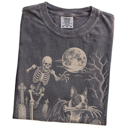 Folded Pepper Comfort Colors® T-shirt showing Boston Terrier running through a moonlit graveyard with a chasing skeleton
