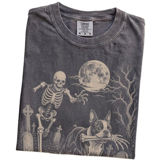 Folded Pepper Comfort Colors® T-shirt showing Boston Terrier running through a moonlit graveyard with a chasing skeleton