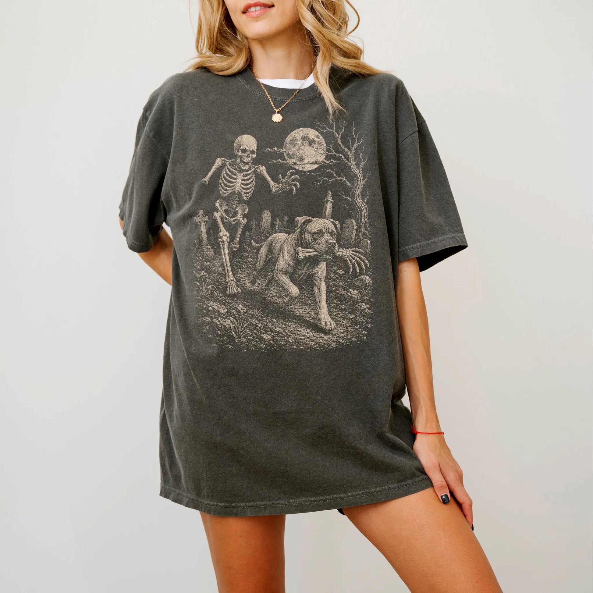 Model wearing a Pepper Comfort Colors® T-shirt showing Cane Corso running through a moonlit graveyard with a chasing skeleton