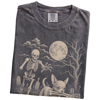 Folded Pepper Comfort Colors® T-shirt showing Chihuahua running through a moonlit graveyard with a chasing skeleton