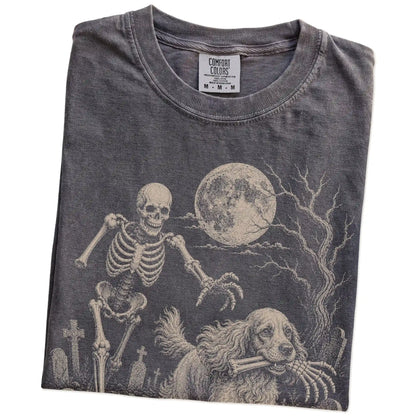 Folded Pepper Comfort Colors® T-shirt showing Cocker Spaniel running through a moonlit graveyard with a chasing skeleton