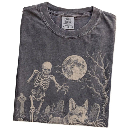 Folded Pepper Comfort Colors® T-shirt showing Corgi running through a moonlit graveyard with a chasing skeleton