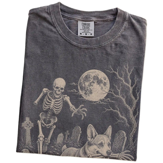 Folded Pepper Comfort Colors® T-shirt showing Corgi running through a moonlit graveyard with a chasing skeleton