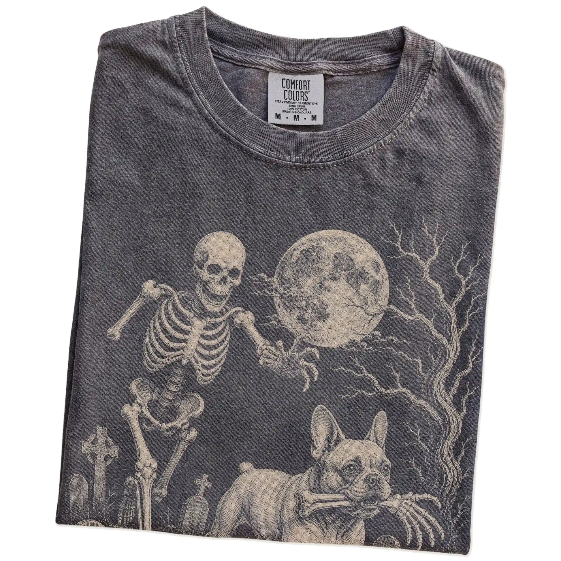 Folded Pepper Comfort Colors® T-shirt showing French Bulldog running through a moonlit graveyard with a chasing skeleton