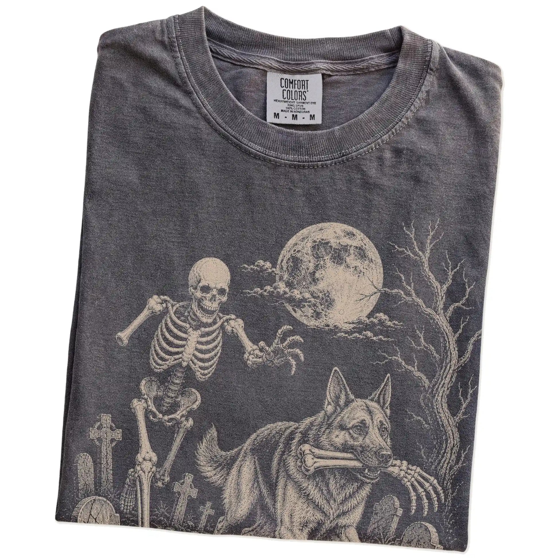 Folded Pepper Comfort Colors® T-shirt showing German Shepherd running through a moonlit graveyard with a chasing skeleton