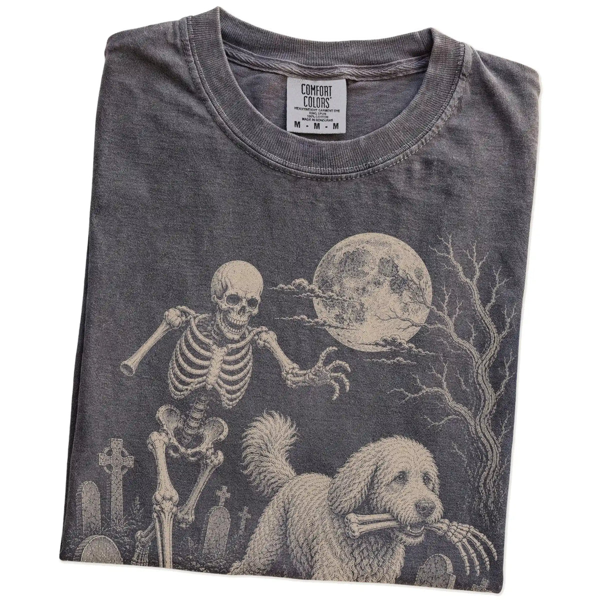 Folded Pepper Comfort Colors® T-shirt showing Goldendoodle running through a moonlit graveyard with a chasing skeleton
