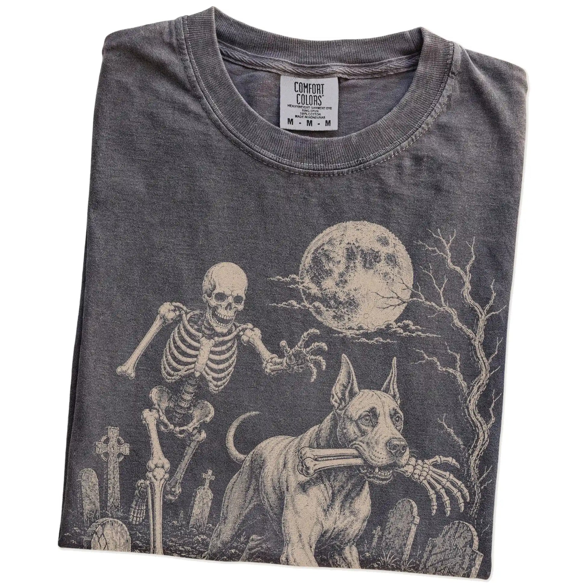 Folded Pepper Comfort Colors® T-shirt showing Great Dane running through a moonlit graveyard with a chasing skeleton