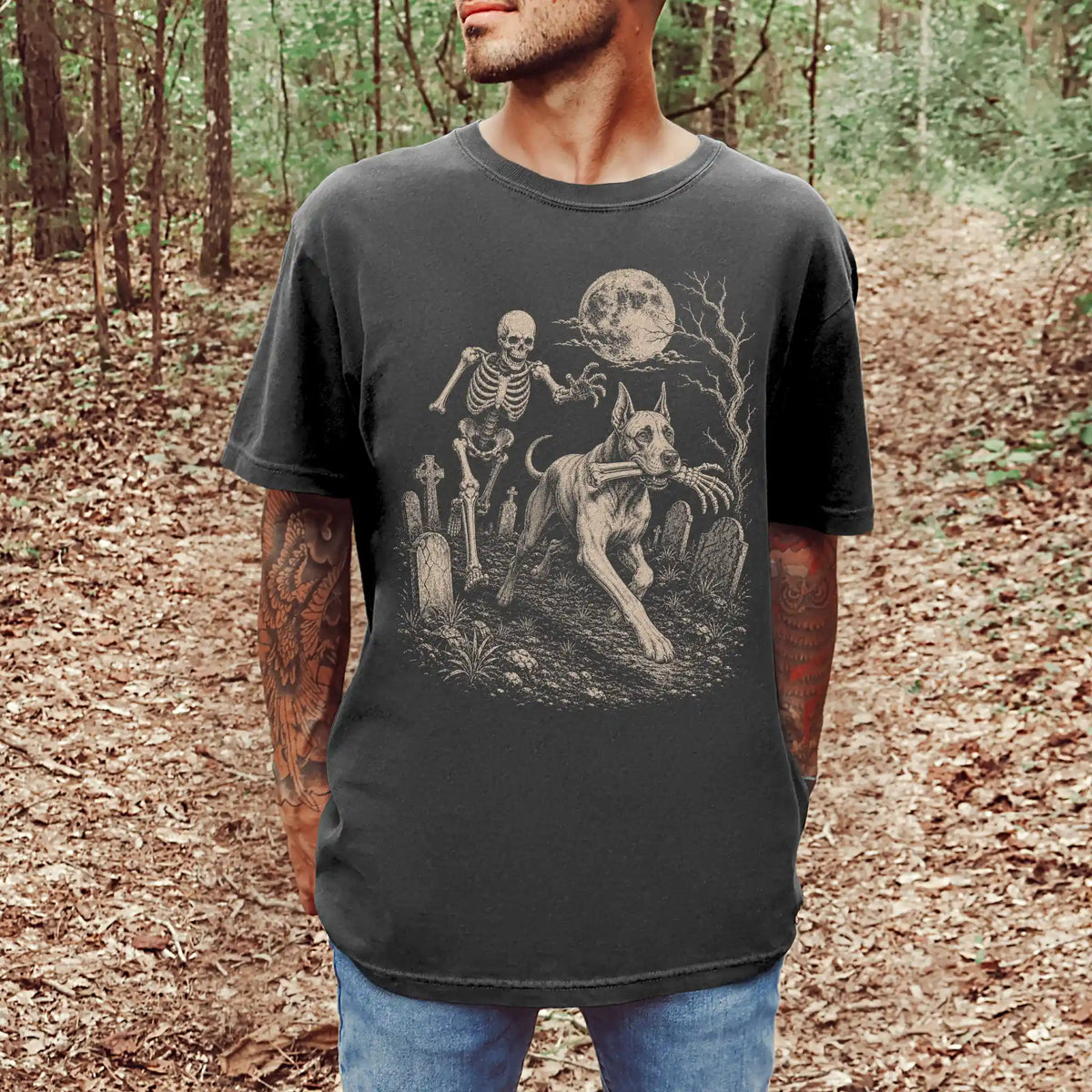 Model wearing a Pepper Comfort Colors® T-shirt showing Great Dane running through a moonlit graveyard with a chasing skeleton