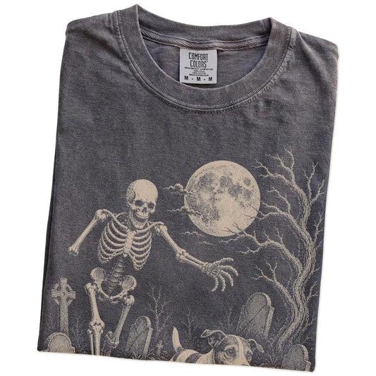 Folded Pepper Comfort Colors® T-shirt showing Jack Russell running through a moonlit graveyard with a chasing skeleton