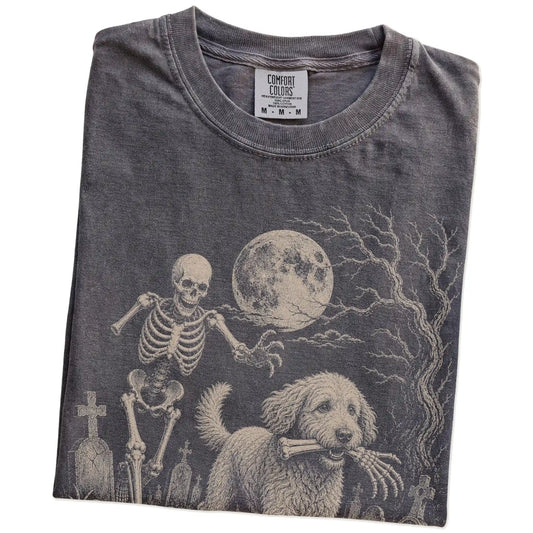 Folded Pepper Comfort Colors® T-shirt showing Labradoodle running through a moonlit graveyard with a chasing skeleton