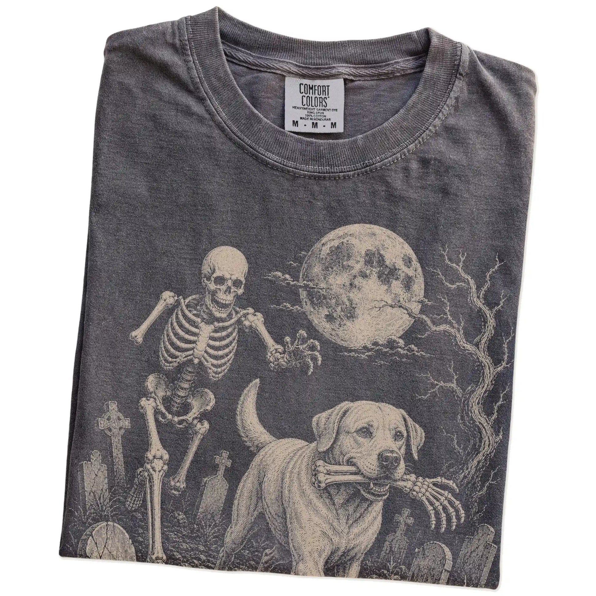 Folded Pepper Comfort Colors® T-shirt showing Labrador Retriever running through a moonlit graveyard with a chasing skeleton