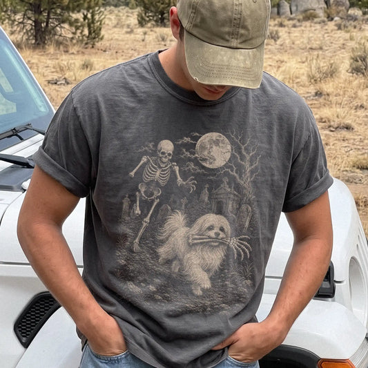 Model wearing a Pepper Comfort Colors® T-shirt showing Maltese running through a moonlit graveyard with a chasing skeleton