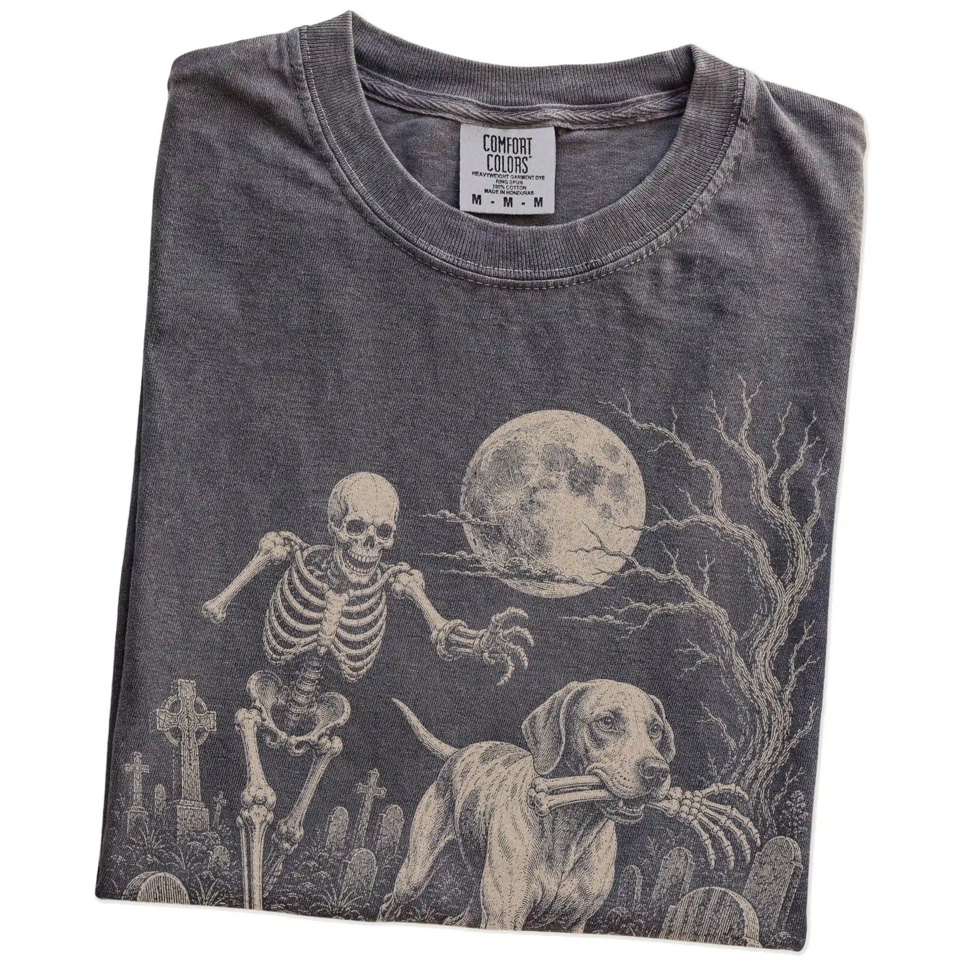 Folded Pepper Comfort Colors® T-shirt showing Pointer running through a moonlit graveyard with a chasing skeleton