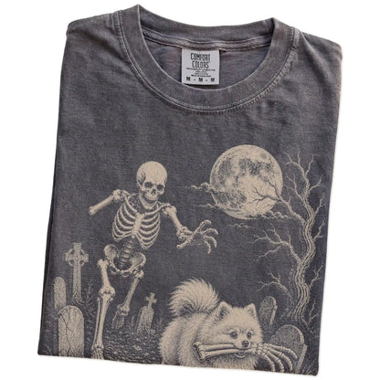 Folded Pepper Comfort Colors® T-shirt showing Pomeranian running through a moonlit graveyard with a chasing skeleton