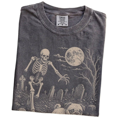 Folded Pepper Comfort Colors® T-shirt showing Pug running through a moonlit graveyard with a chasing skeleton