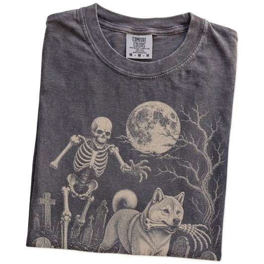 Folded Pepper Comfort Colors® T-shirt showing Shiba Inu running through a moonlit graveyard with a chasing skeleton