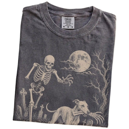 Folded Pepper Comfort Colors® T-shirt showing Whippet running through a moonlit graveyard with a chasing skeleton