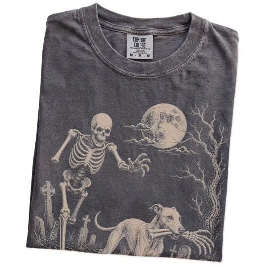 Folded Pepper Comfort Colors® T-shirt showing Whippet running through a moonlit graveyard with a chasing skeleton
