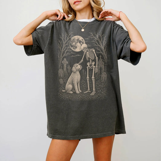 Model wearing a Pepper Comfort Colors® T-shirt showing Labradoodle sharing a quiet cemetery moment with a friendly skeleton