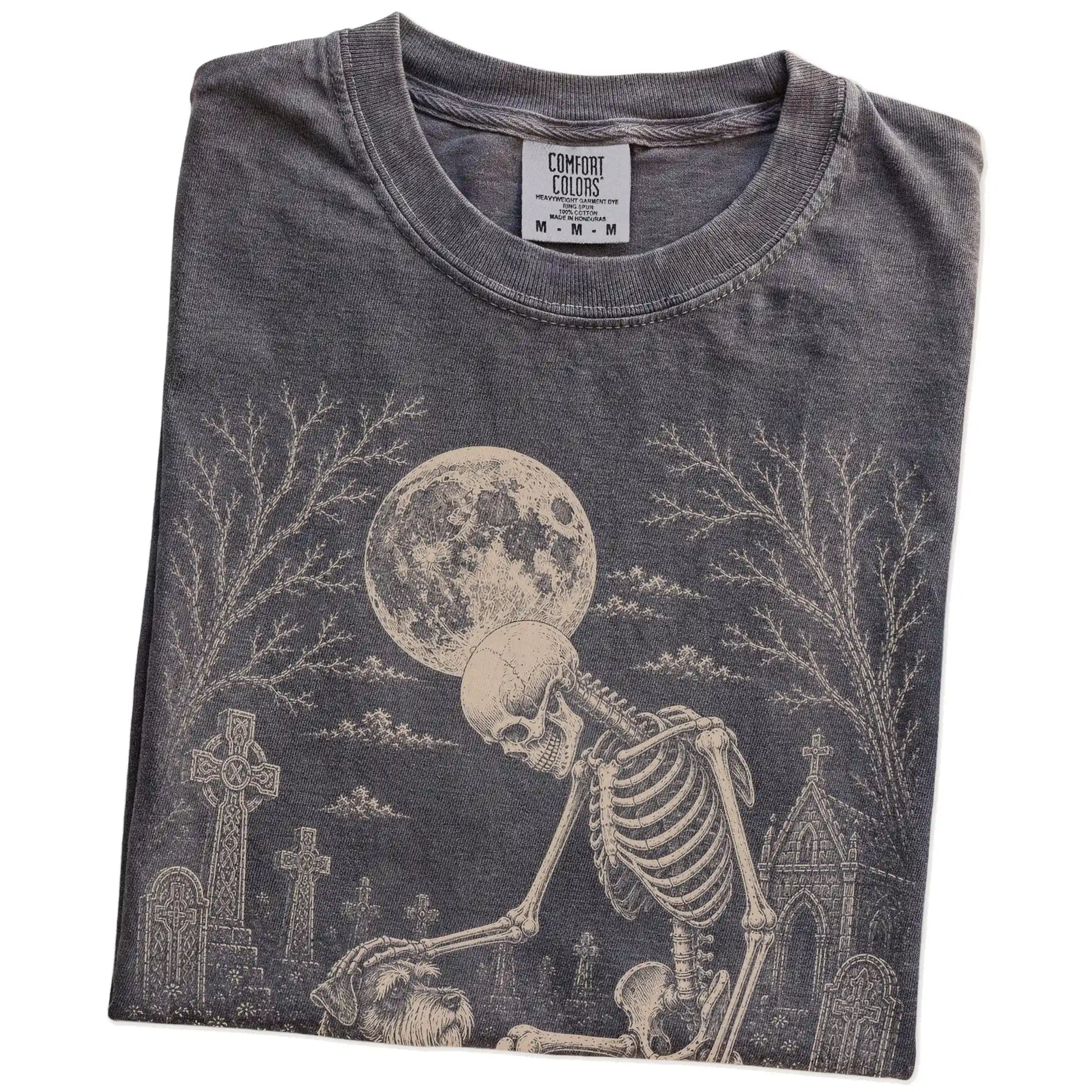 Folded Pepper Comfort Colors® T-shirt showing Schnauzer sharing a quiet cemetery moment with a friendly skeleton