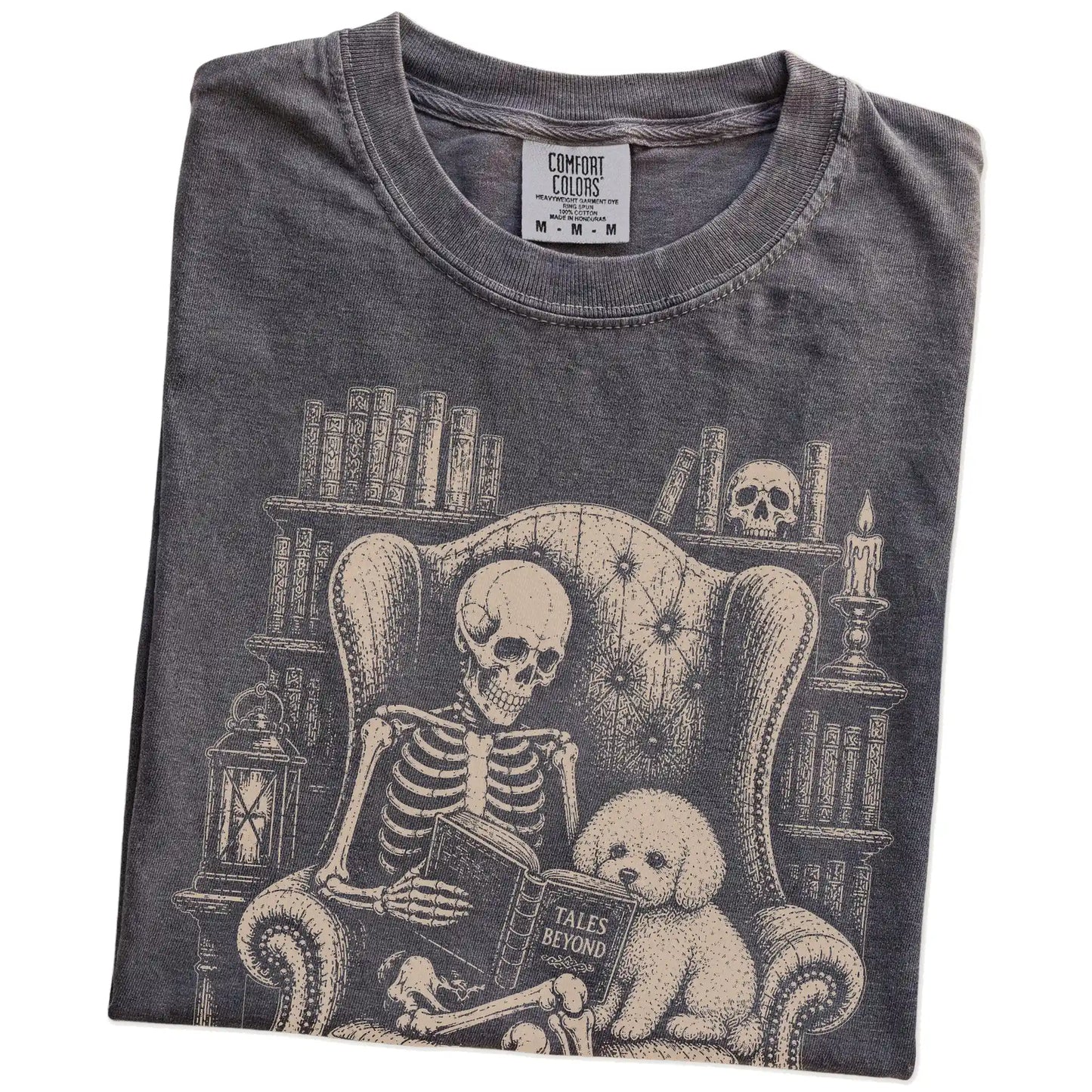 Folded Pepper Comfort Colors® T-shirt showing skeleton reading in a library beside a Bichon Frise