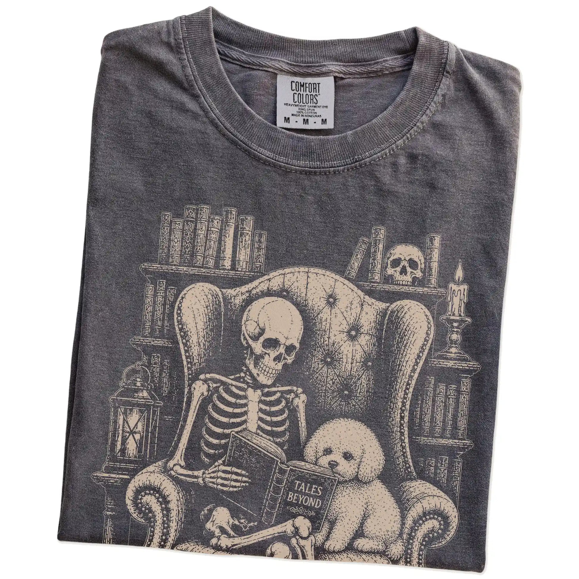 Folded Pepper Comfort Colors® T-shirt showing skeleton reading in a library beside a Bichon Frise