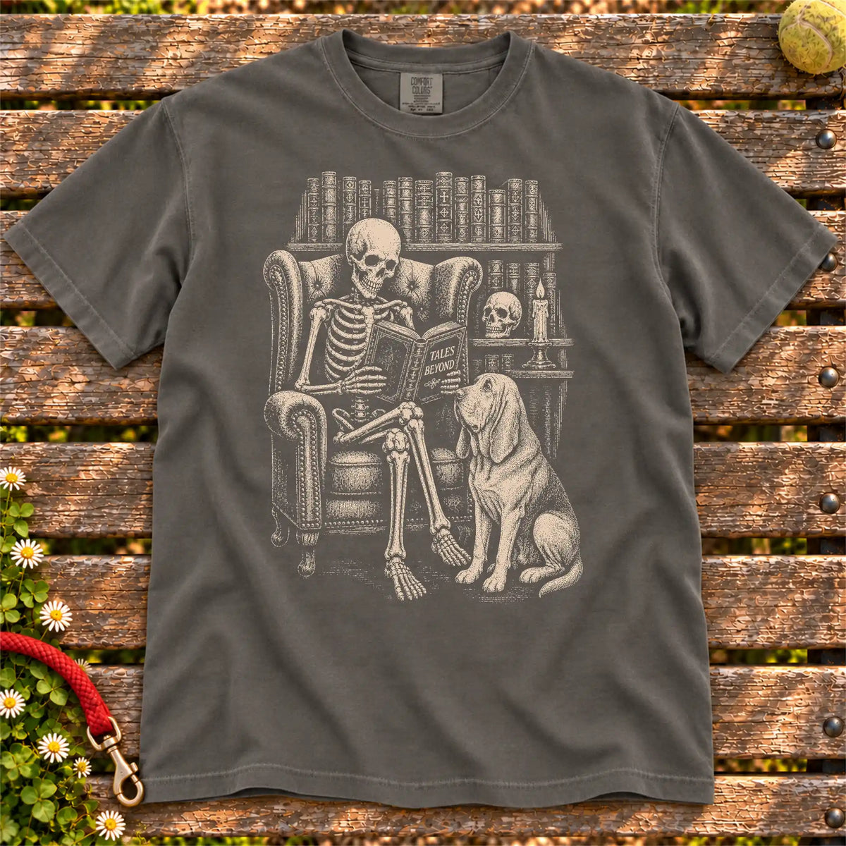 Skeleton reading in a library beside a Bloodhound on a Pepper Comfort Colors® T-shirt