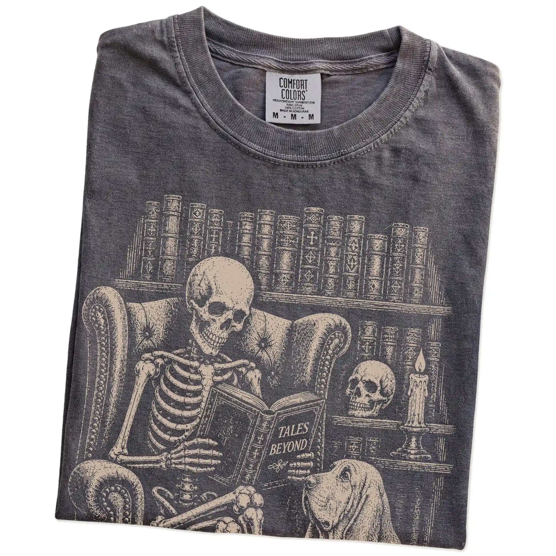 Folded Pepper Comfort Colors® T-shirt showing skeleton reading in a library beside a Bloodhound
