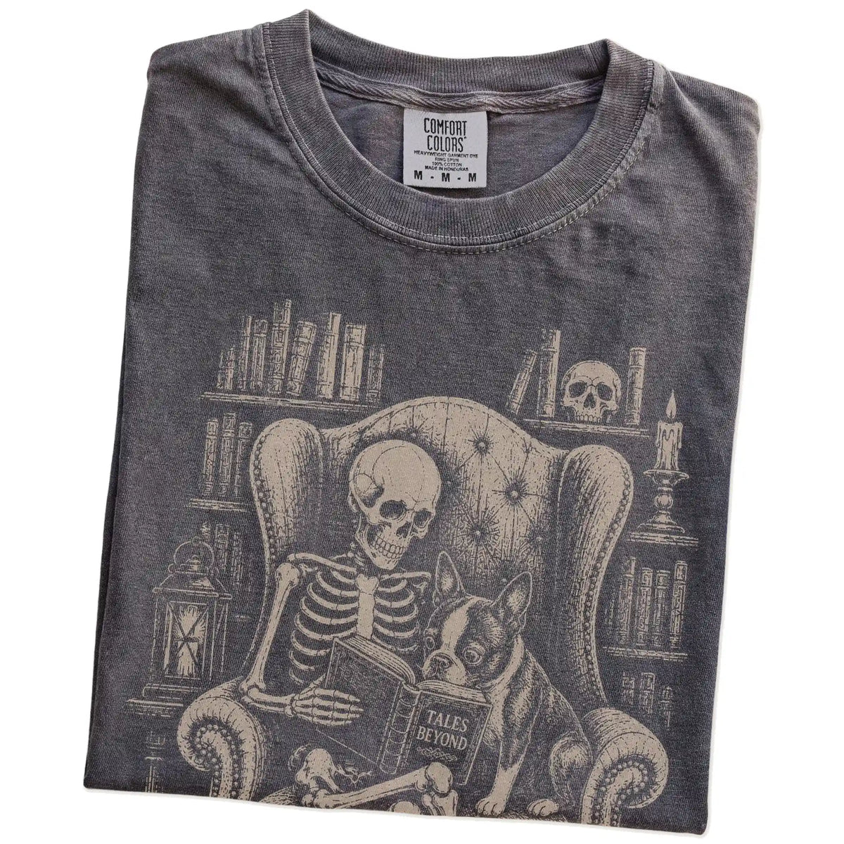 Folded Pepper Comfort Colors® T-shirt showing skeleton reading in a library beside a Boston Terrier