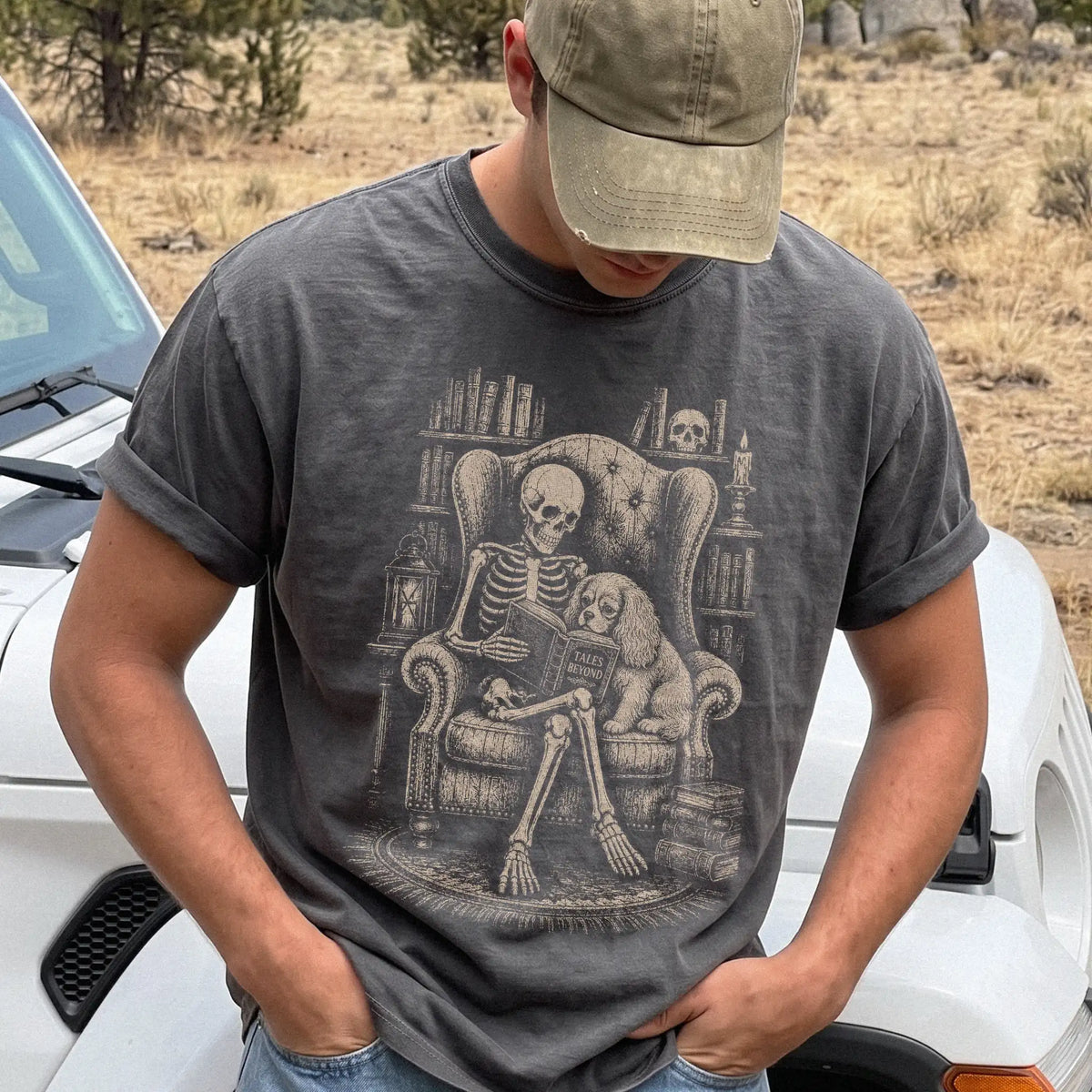 Model wearing a Pepper Comfort Colors® T-shirt showing skeleton reading in a library beside a Cavalier King Charles Spaniel