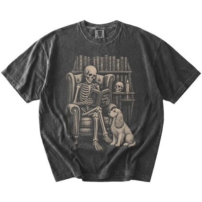 Skeleton reading in a library beside a Cocker Spaniel on a Pepper Comfort Colors® T-shirt