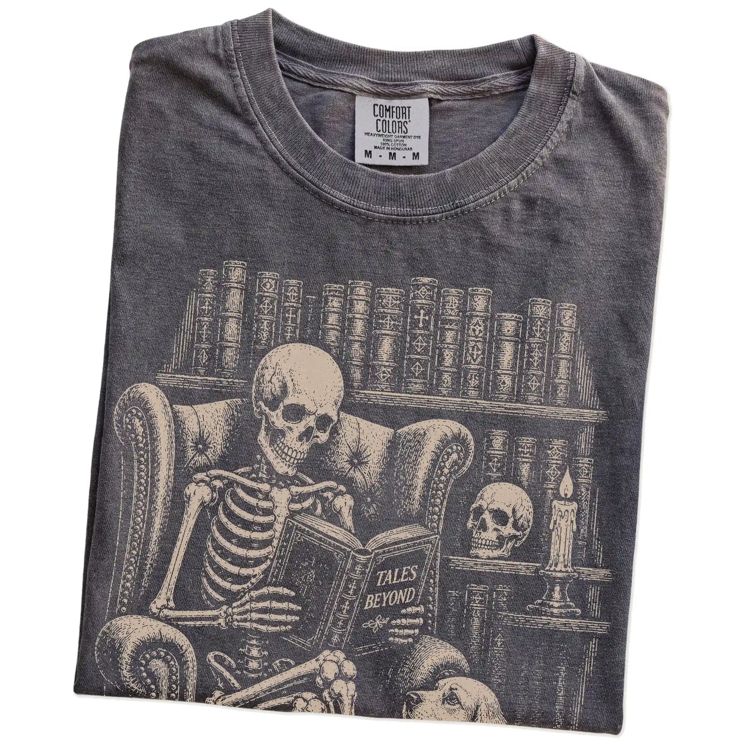 Folded Pepper Comfort Colors® T-shirt showing skeleton reading in a library beside a Cocker Spaniel