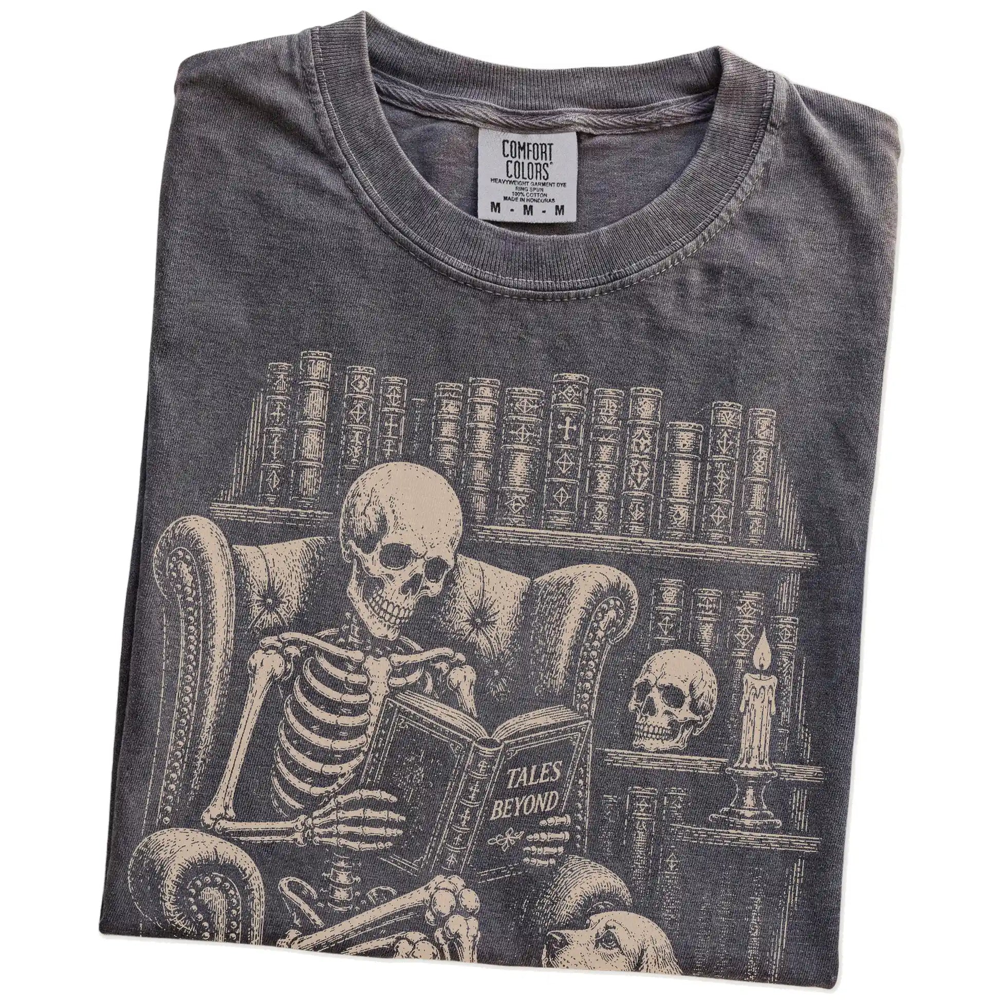 Folded Pepper Comfort Colors® T-shirt showing skeleton reading in a library beside a Cocker Spaniel