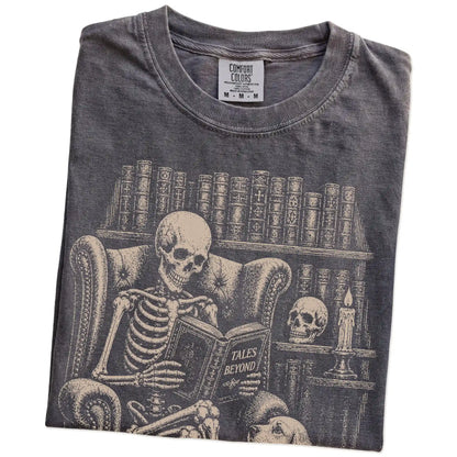 Folded Pepper Comfort Colors® T-shirt showing skeleton reading in a library beside a Cocker Spaniel