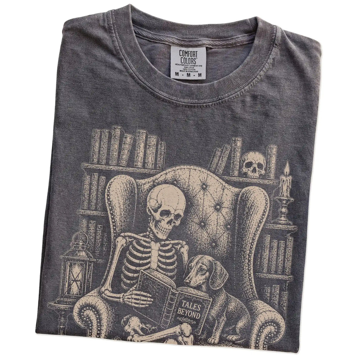 Folded Pepper Comfort Colors® T-shirt showing skeleton reading in a library beside a Dachshund