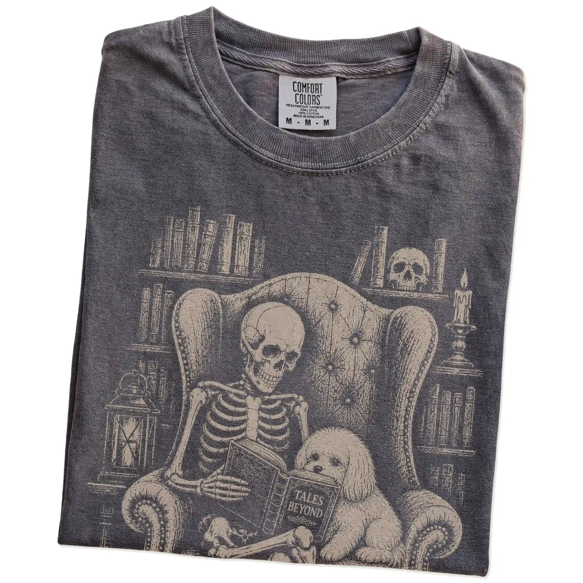 Folded Pepper Comfort Colors® T-shirt showing skeleton reading in a library beside a Maltese