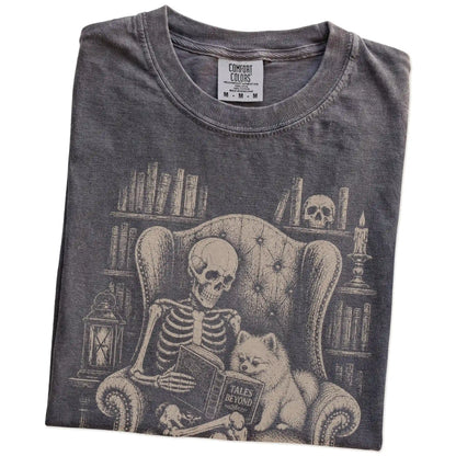 Folded Pepper Comfort Colors® T-shirt showing skeleton reading in a library beside a Pomeranian
