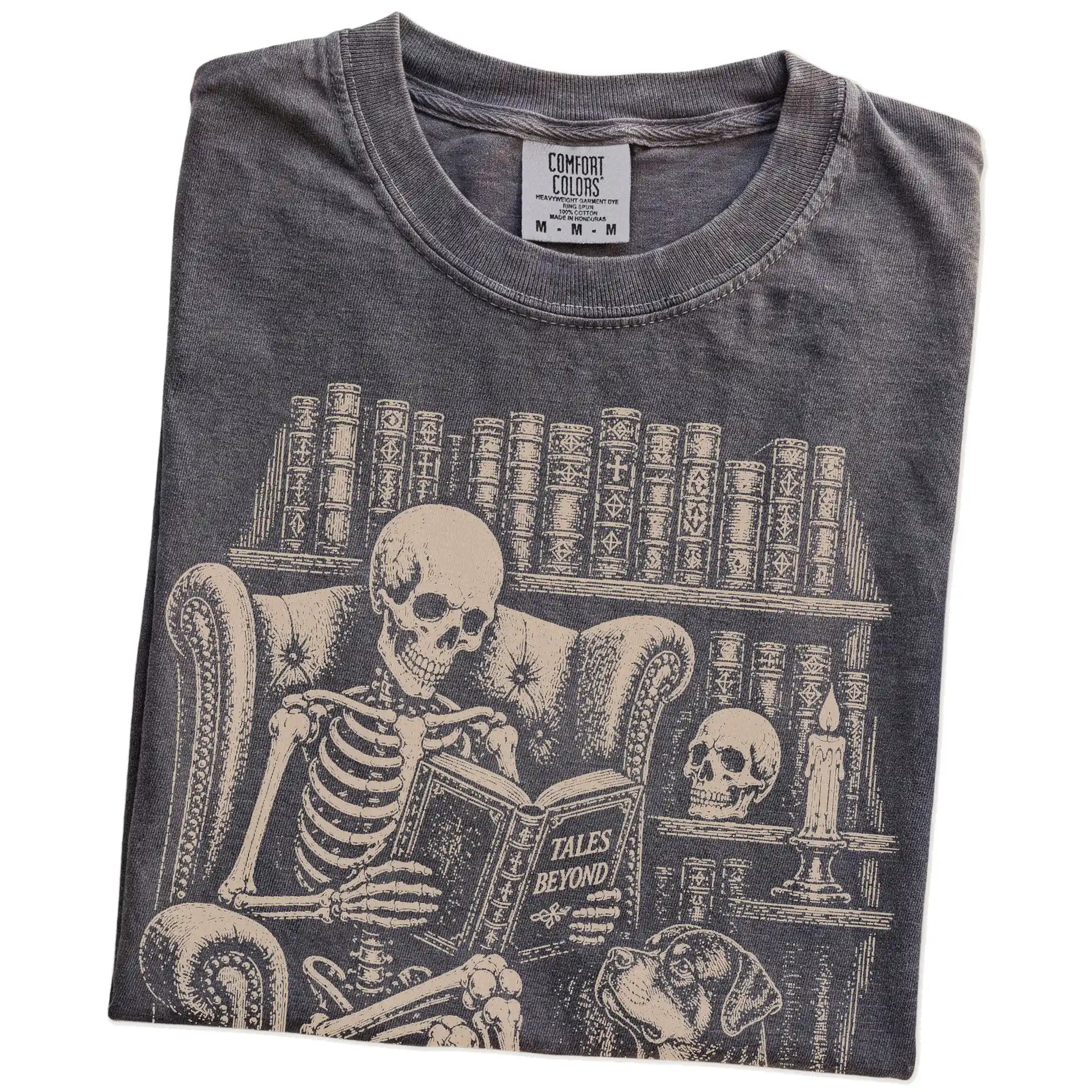 Folded Pepper Comfort Colors® T-shirt showing skeleton reading in a library beside a Rottweiler