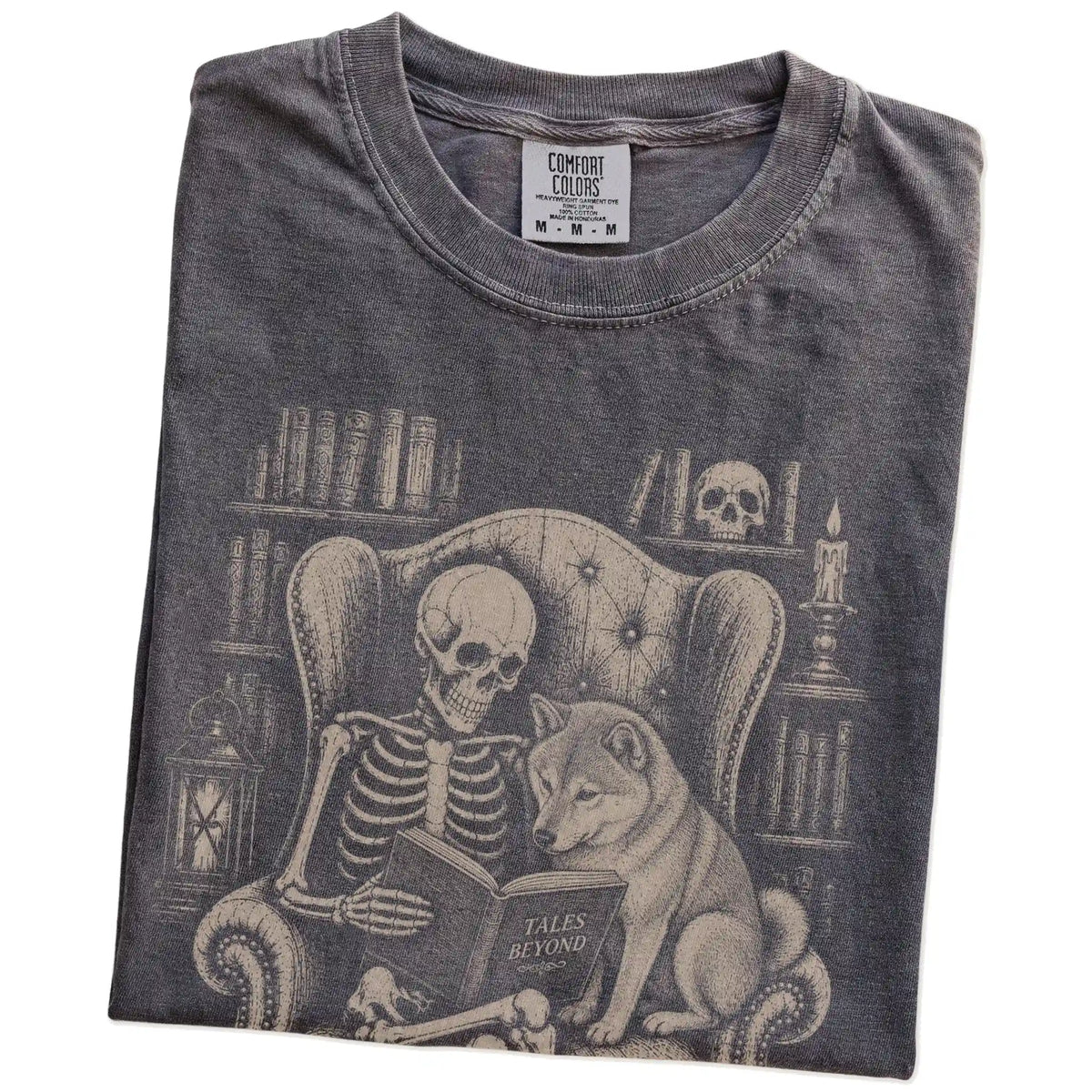 Folded Pepper Comfort Colors® T-shirt showing skeleton reading in a library beside a Shiba Inu