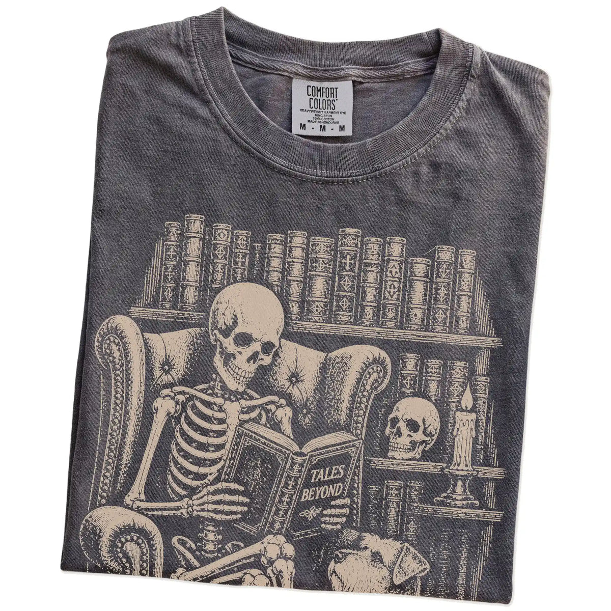 Folded Pepper Comfort Colors® T-shirt showing skeleton reading in a library beside a Schnauzer