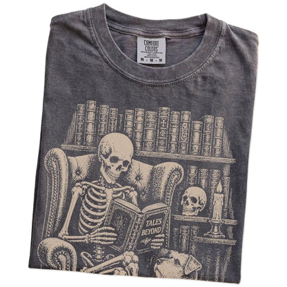 Folded Pepper Comfort Colors® T-shirt showing skeleton reading in a library beside a Schnauzer