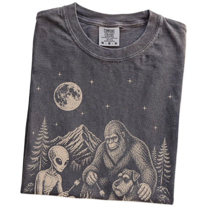 Folded Pepper Comfort Colors® T-shirt showing Standard Schnauzer camping with Bigfoot and an alien