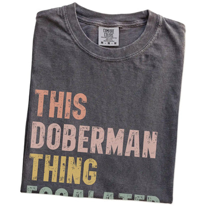 Folded Pepper Comfort Colors® T-shirt showing retro “This Doberman Thing Escalated Quickly” lettering
