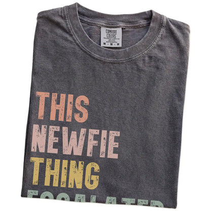 Folded Pepper Comfort Colors® T-shirt showing retro “This Newfie Thing Escalated Quickly” lettering