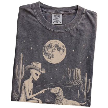 Folded Pepper Comfort Colors® T-shirt showing cowboy alien fist-bumping a vizsla beneath the moon