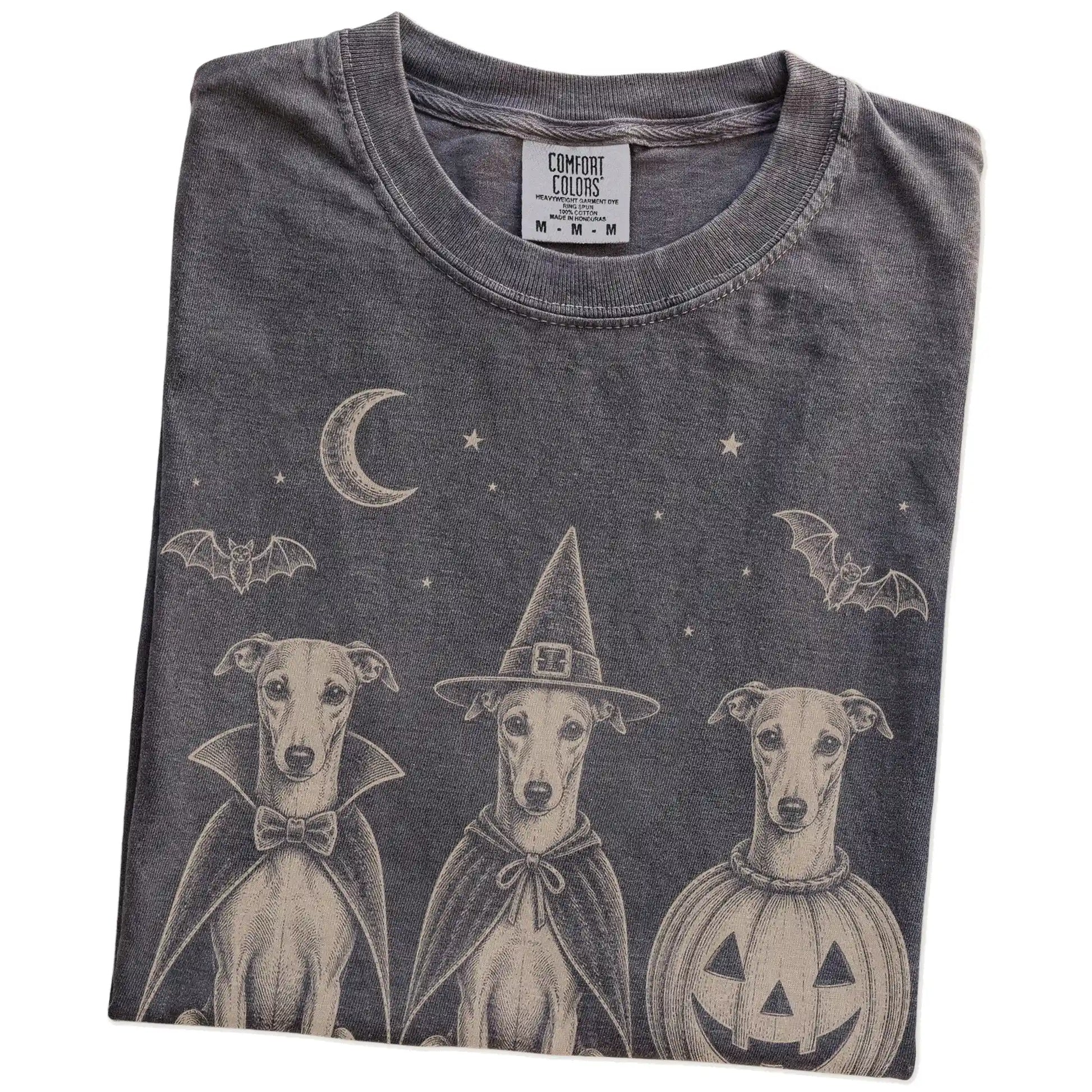 Folded Pepper Comfort Colors® T-shirt showing three Whippet dogs dressed for Halloween beneath bats and a crescent moon