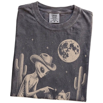 Folded Pepper Comfort Colors® T-shirt showing cowboy alien fist-bumping a yorkie beneath the moon