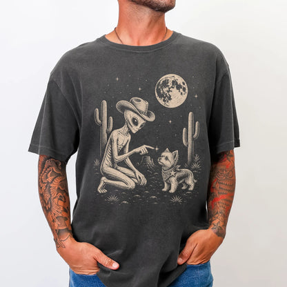 Model wearing a Pepper Comfort Colors® T-shirt with cowboy alien fist-bumping a yorkie beneath the moon