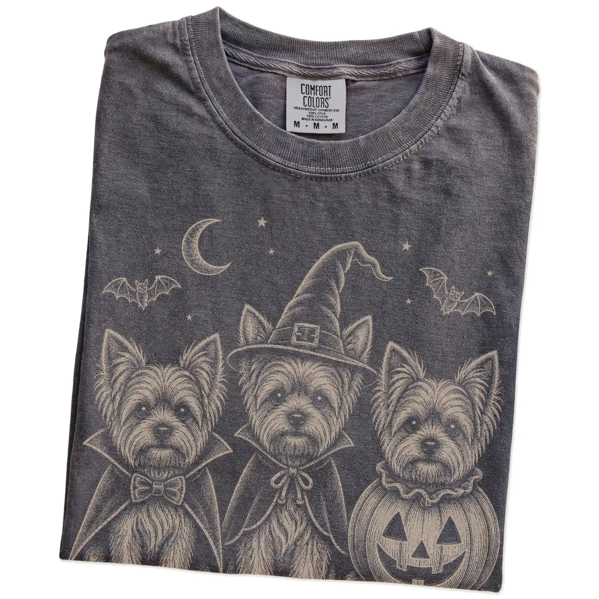 Folded Pepper Comfort Colors® T-shirt showing three Yorkie dogs dressed for Halloween beneath bats and a crescent moon