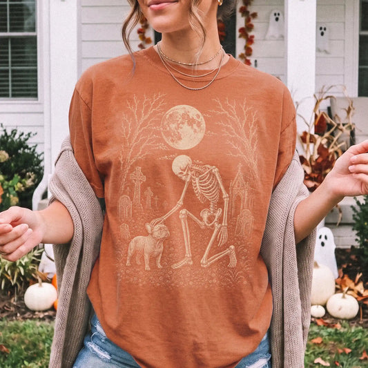 Model wearing a Yam Comfort Colors® T-shirt showing French Bulldog sharing a quiet cemetery moment with a friendly skeleton